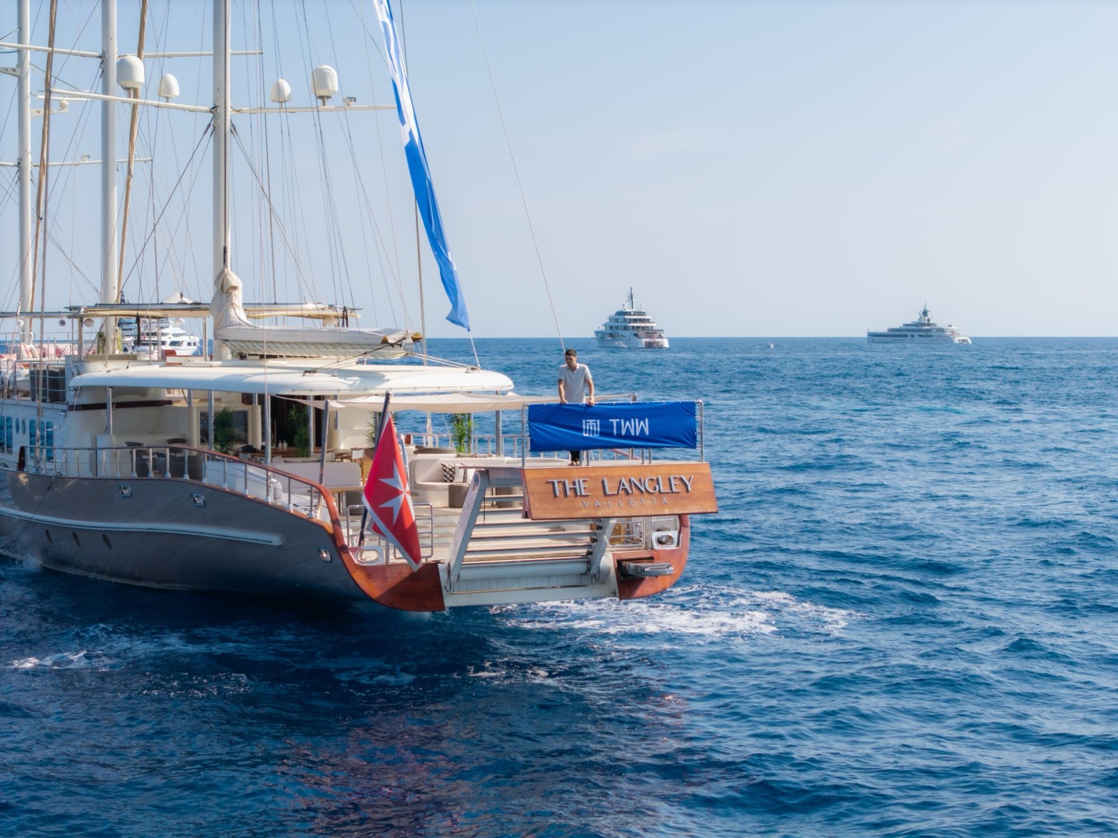 Jerome Kwamo an Bord einer Segelyacht auf See, im Hintergrund zwei Superyachten